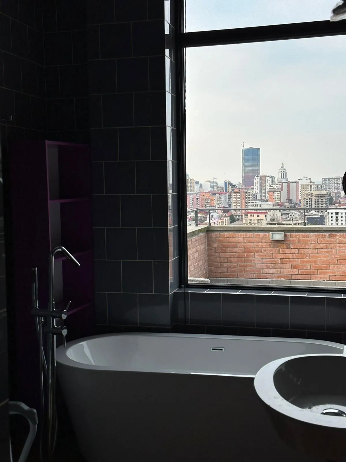 Freestanding bathtub beside a window overlooking the city