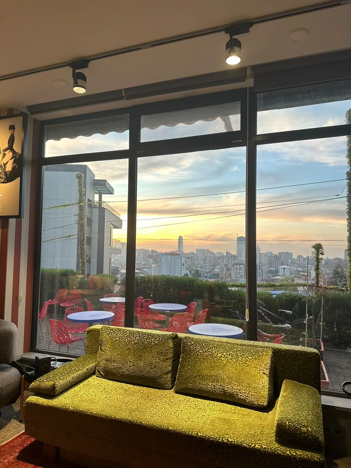 A velvet sofa facing floor-to-ceiling windows and a sunset over the city