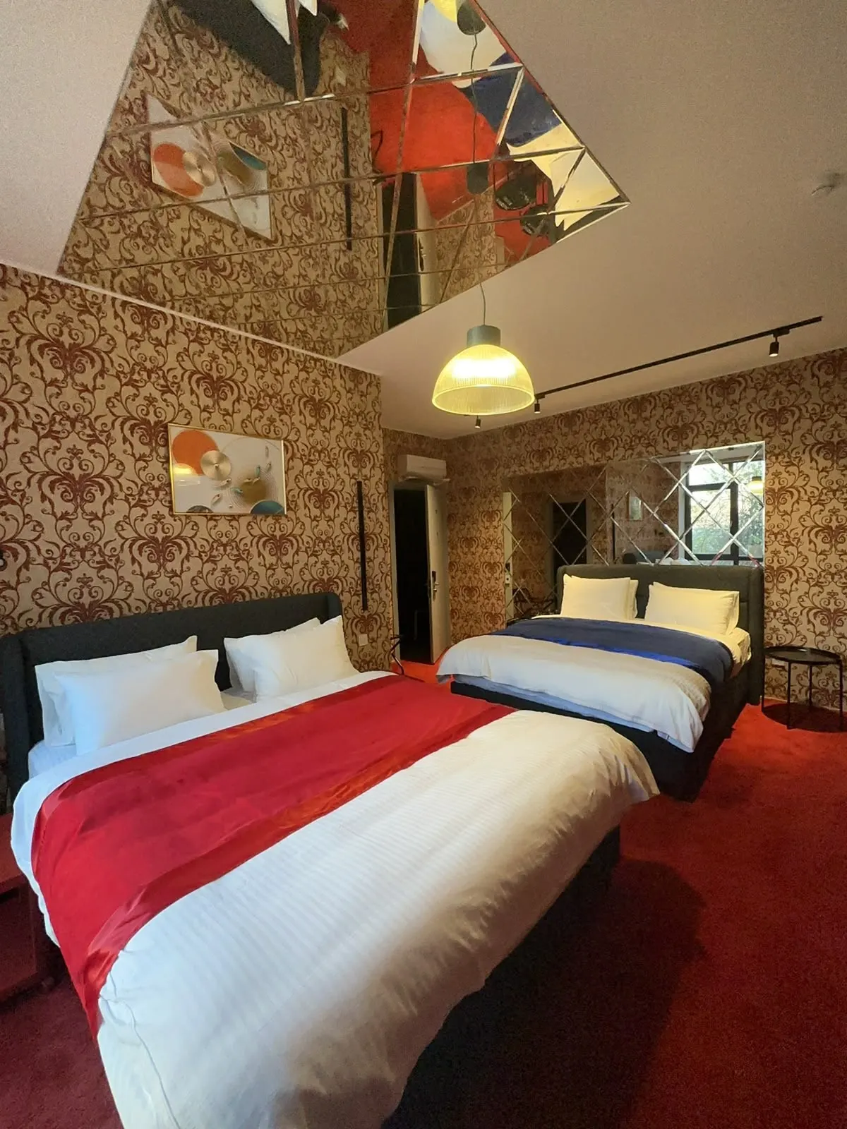 Guest room with patterned wallpaper, a mirrored ceiling and red bedding